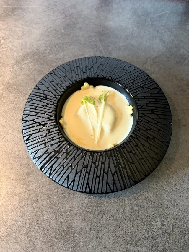 Petite préparation ronde à la crème jaune, dressée sur une assiette noire texturée.