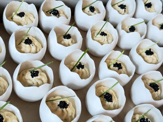 Bouchées crémeuses présentées dans des coquilles blanches, avec une garniture sombre et des brins verts.