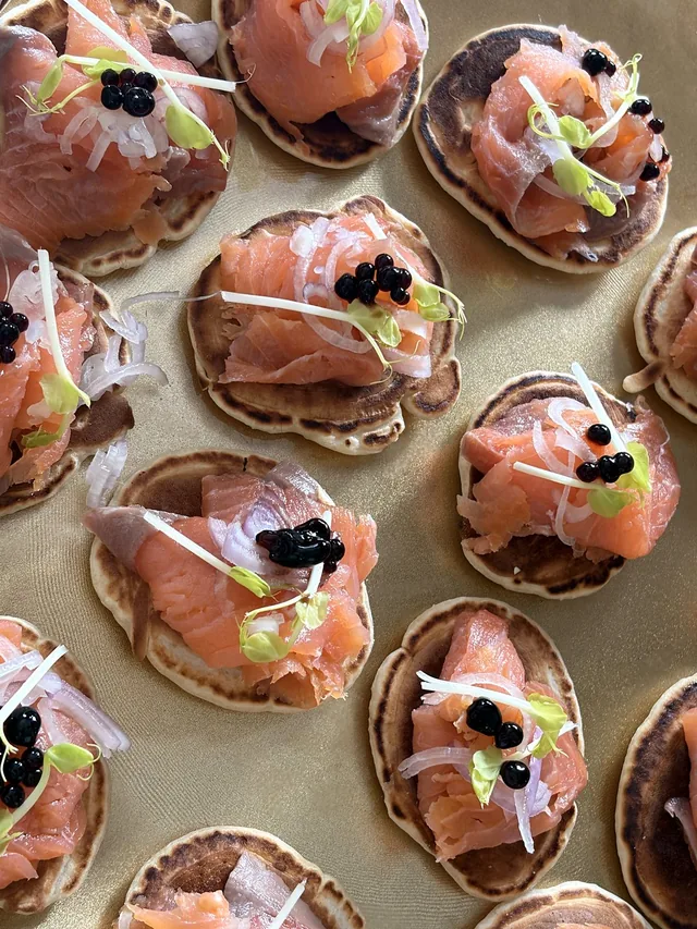 Canapés au saumon disposés sur un plateau, garnis de jeunes pousses et de petites perles sombres.