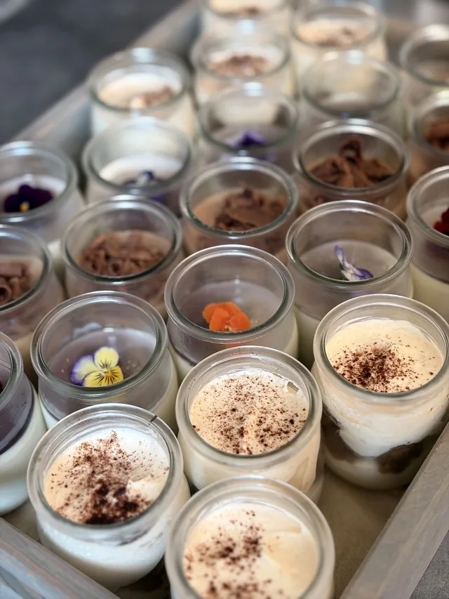 Assortiment de petites verrines aux préparations claires et brunes, disposées en rangées.