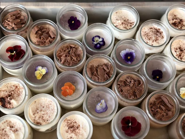 Vue de dessus d’un assortiment de verrines décorées de fleurs colorées, de copeaux et de poudre brune.